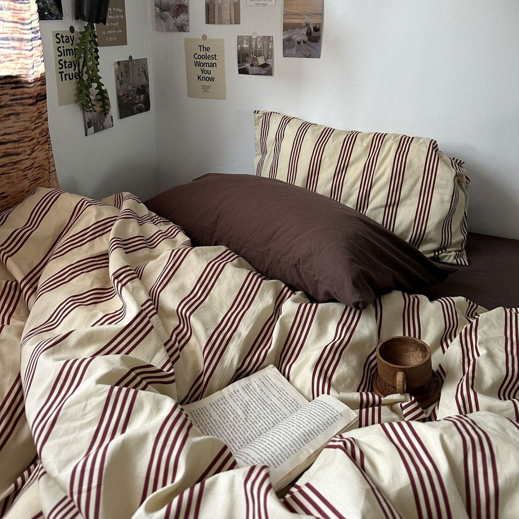 Bed with striped bedding and pillows, featuring a book and wooden cup.