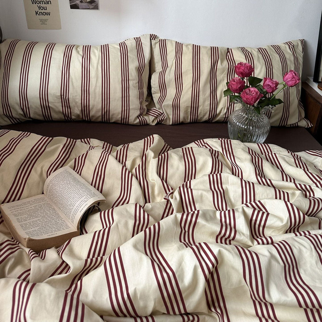 Bed with striped bedding, open book, and vase of flowers on a wooden nightstand.